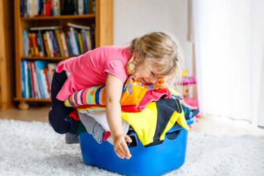 Büyük bir sepet dolusu temiz çamaşırları olan küçük kız ütüye hazır. Mutlu güzel bebek ve bebek anne ev işlerine ve kıyafetlere yardım ediyor..