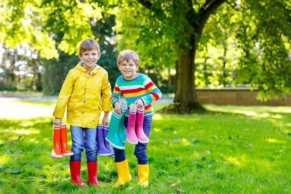 Two little kids boys, cute siblings with lots of colorful rain boots. Children in different rubber boots and jackets. Footwear for rainy fall. Healthy twins and best friends having fun outdoors — Stock Photo, Image