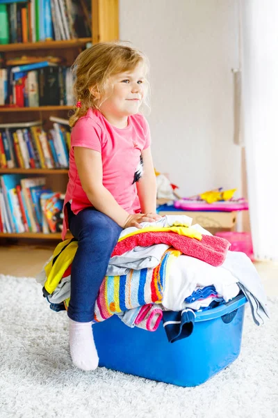 Niña con una gran cesta de ropa limpia y fresca lista para planchar. Feliz hermoso niño y bebé hija ayudando a la madre con las tareas domésticas y la ropa. — Foto de Stock
