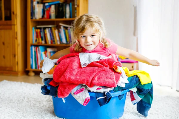 Niña con una gran cesta de ropa limpia y fresca lista para planchar. Feliz hermoso niño y bebé hija ayudando a la madre con las tareas domésticas y la ropa. — Foto de Stock