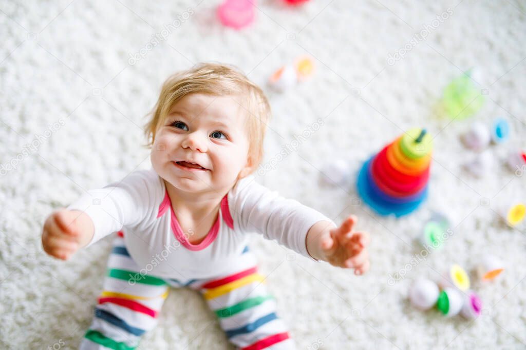 Adorable cute beautiful little baby girl playing with educational toys at home or nursery. Happy healthy child having fun with colorful wooden rainboy toy pyramid. Kid learning different skills.