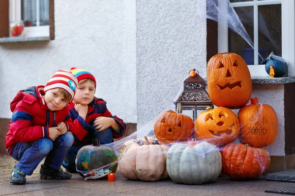 Zwei kleine Jungen sitzen mit traditionellen Jack-o-Laternen-Kürbissen zu Halloween vor der geschmückten Gruseltür im Freien. Kinder haben Spaß und feiern Ferien — Stockfoto