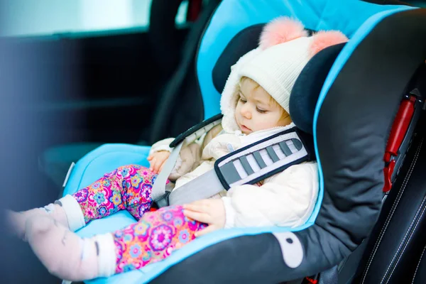 En söt liten flicka med blå ögon som sitter i bilsätet. Leksaksbarn i vinterkläder åker på familjesemester och jorney. Säker resa, barnsäkerhet, transportkoncept. — Stockfoto