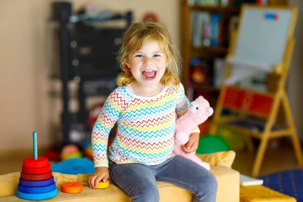 Menina pequena bonito brincando sozinho com pirâmide de arco-íris de madeira colorido e brinquedos em casa ou berçário. Criança saudável feliz se divertindo no jardim de infância ou creche pré-escolar — Fotografia de Stock