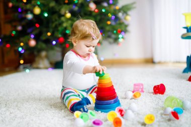 Evde ya da çocuk odasında eğitici oyuncaklarla oynayan sevimli, güzel bir kız bebek. Mutlu sağlıklı çocuk renkli ahşap çocuk oyuncak piramidiyle eğleniyor. Çocuk farklı yetenekler öğreniyor.