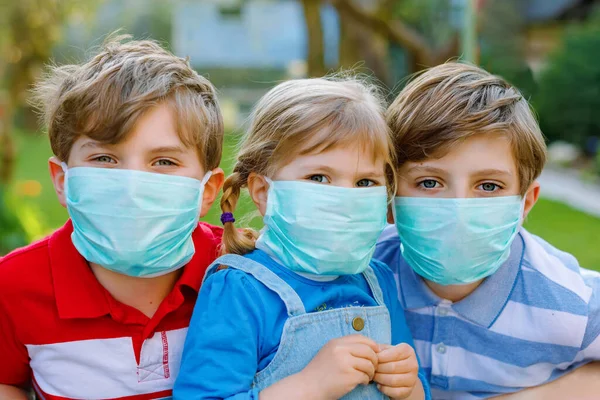 Tres niños, una niña pequeña y dos niños con máscara médica como protección contra la enfermedad por coronavirus pandémica. Niños, hermanos encantadores usando equipo de protección como lucha contra covid 19. — Foto de Stock