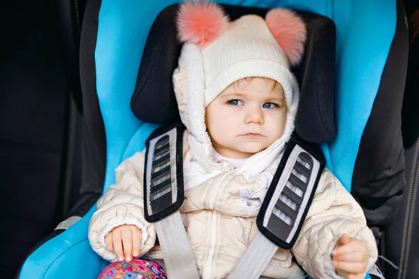 Urocza dziewczynka z niebieskimi oczami siedząca w foteliku samochodowym. Dziecko w zimowych ciuchach jedzie na rodzinne wakacje i do Jorneya. Bezpieczna podróż, bezpieczeństwo dzieci, koncepcja transportu. — Zdjęcie stockowe
