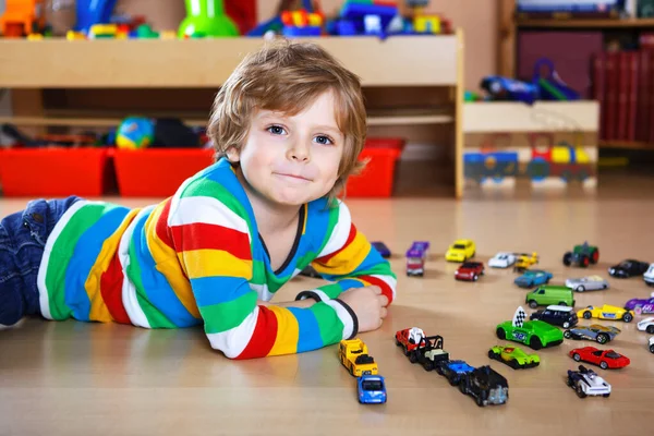 Υπέροχο ξανθό αγόρι που παίζει με πολλά αυτοκινητάκια. Ευτυχισμένο υγιές παιδί που περνάει καλά κατά τη διάρκεια της πανδημικής καραντίνας. Παιδί μόνο στο σπίτι, κλειστό νηπιαγωγείο. — Φωτογραφία Αρχείου