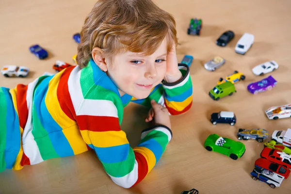 Härligt blond pojke leker med massor av leksaksbilar inomhus. Glad frisk pojke som har roligt under en pandemisk karantänsjukdom. Ensamstående barn hemma, stängd barnkammare. — Stockfoto