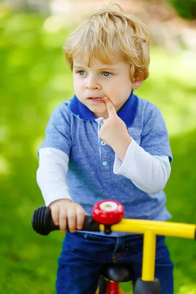 Active blond kid boy in colorful clothes driving balance and learners bike or bicycle in domestic garden. Toddler child dreaming and having fun on warm summer day. outdoors movement game for children — Stock Photo, Image