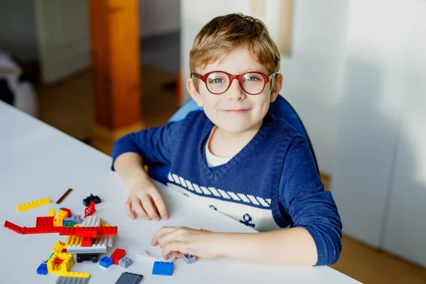 Criança loira com óculos de olho brincando com muitos blocos de plástico coloridos. Menino da escola adorável se divertindo com a construção e criação de robô. Lazer criativo moderno técnico e robótico. — Fotografia de Stock