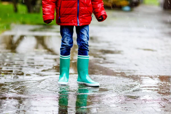 Primer plano del niño con botas de lluvia amarillas y caminando durante el aguanieve, la lluvia y la nieve en el día frío. Niño en ropa casual de moda colorida saltando en un charco. Divertirse al aire libre —  Fotos de Stock