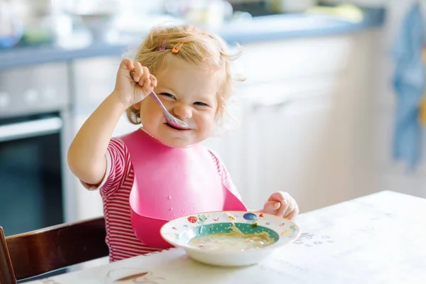 Menina adorável comendo de sopa de macarrão vegetal colher. conceito de alimentação, criança, alimentação e desenvolvimento. Criança bonito, filha com colher sentada em cadeira alta e aprendendo a comer por si só — Fotografia de Stock