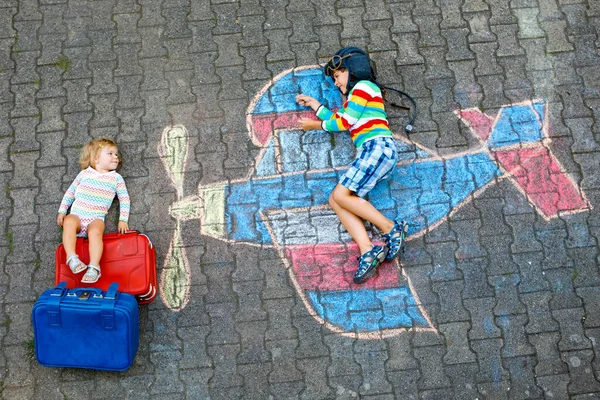 Due bambini piccoli, bambino ragazzo e bambina si divertono con con disegno aereo con gessetti colorati su asfalto. Fratelli che dipingono con il gesso e vanno in vacanza . — Foto Stock