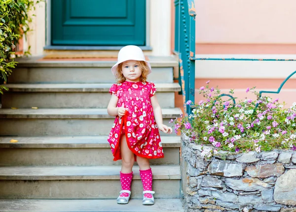 Retrato de hermosa niña preciosa gorgeus en rosa ropa de verano, vestido de moda, calcetines de rodilla y sombrero. Feliz bebé sano posando frente a la casa colorida. —  Fotos de Stock