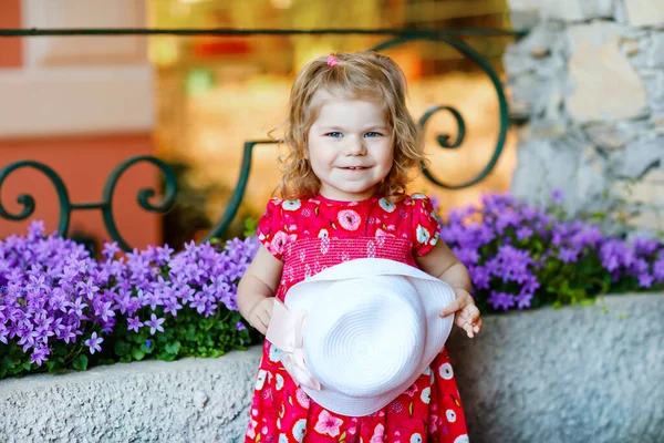 Portrét krásné malé nádherný batole dívka v růžové letní vzhled oblečení, módní šaty, kolena ponožky a klobouk. Šťastné zdravé dítě pózuje před barevným domem. — Stock fotografie