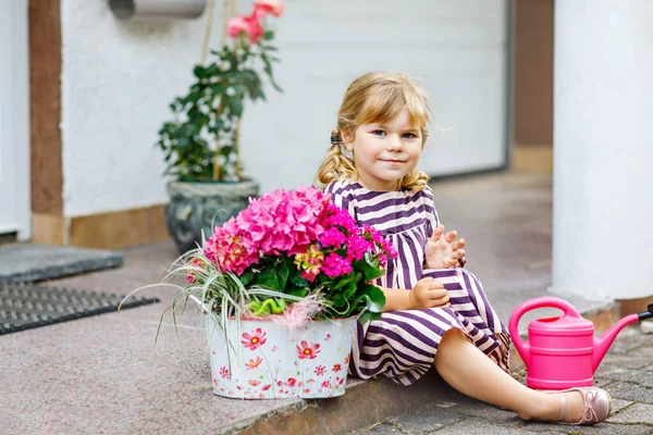 可愛くて魅力的な幼児の少女の肖像画が花と一緒に家に座っている。カラフルな花で夏の日に幸せな赤ちゃんの笑顔、屋外。幸せと夏. — ストック写真