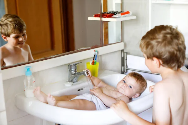 Cute adorable baby taking bath in washing sink and grab water tap. Kid boy helping and playing with sister. Happy brother and child having fun. Healthy children in bathroom together. Family time. — Stock Photo, Image