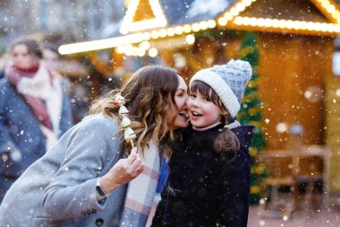 Anne ve kızı geleneksel Alman Noel pazarında beyaz çikolata kaplı meyve ve çilek yiyorlar. Karlı bir günde Almanya 'da geleneksel aile pazarında mutlu kız ve kadın