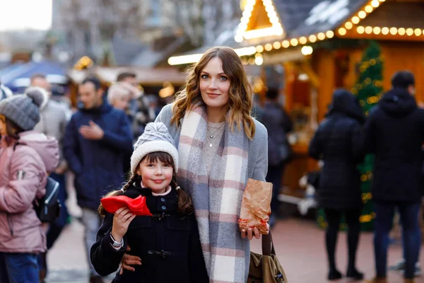 Mother and daughter eating white chocolate covered fruits and strawberry on skewer on traditional German Christmas market. Happy girl and woman on traditional family market in Germany during snowy day — Stock Photo, Image