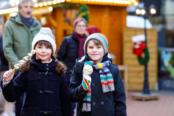 Küçük tatlı kız ve oğlan geleneksel Alman Noel pazarında beyaz çikolata kaplı çilek ve elma yiyorlar. Mutlu çocuklar, en iyi arkadaşlar, ikizler ve kardeşler karlı bir günde — Stok fotoğraf