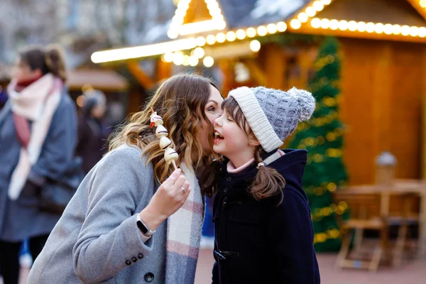 Mère et fille mangeant des fruits couverts de chocolat blanc et fraise sur brochette sur le marché de Noël allemand traditionnel. Fille heureuse et femme sur le marché familial traditionnel en Allemagne pendant la journée enneigée — Photo