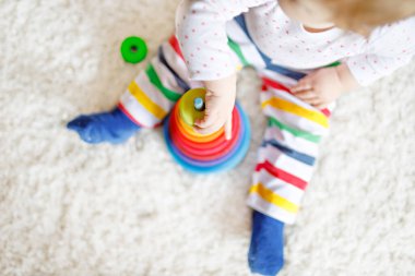 Evde ya da çocuk odasında eğitici oyuncaklarla oynayan sevimli, güzel bir kız bebek. Mutlu sağlıklı çocuk renkli ahşap çocuk oyuncak piramidiyle eğleniyor. Çocuk farklı yetenekler öğreniyor