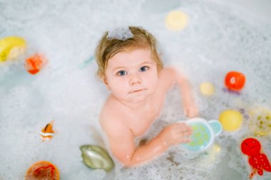 Küvette köpüklü banyo yapan sevimli, sevimli bir kız. Bebek banyo lastiği oyuncaklarıyla oynuyor. Güzel çocuk renkli sakız oyuncakları ve köpüklerle eğleniyor.