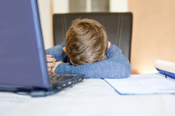 Грустный уставший мальчик делает домашнее задание и учится дома с ноутбуком. Заинтересованный ребенок пишет эссе с помощью Интернета. сокрытие школьников и концепция домашнего обучения — стоковое фото