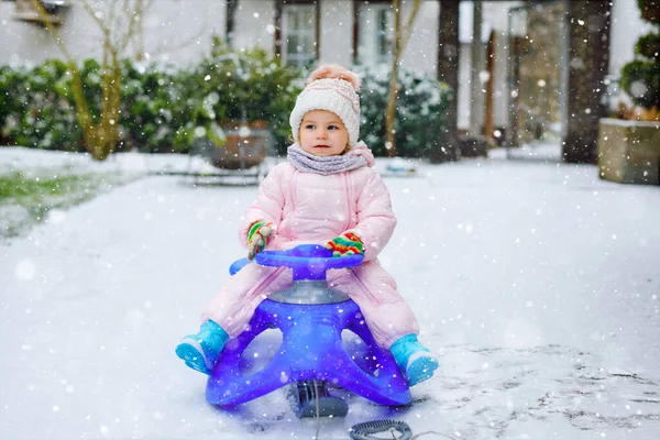 Söt liten småbarn flicka njuter av en släde rida på snö. Barnspann. Baby kid rider en släde i färgglada mode kläder. Utomhus aktivt roligt för familjen vintersemester på dagen med snöfall — Stockfoto