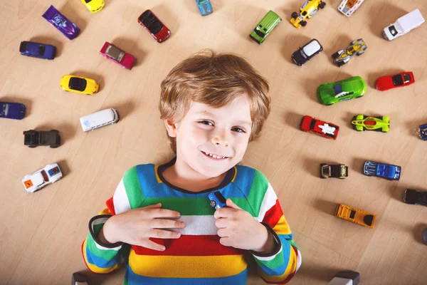 Menino loiro encantador brincando com muitos carros de brinquedo no interior. Menino saudável feliz se divertindo durante a doença de quarentena do coronavírus pandêmico. Criança sozinha em casa, berçário fechado. — Fotografia de Stock