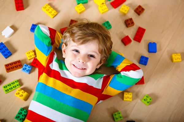 Piccolo bambino biondo che gioca con un sacco di blocchi di plastica colorati al coperto. Ragazzo che indossa camicia colorata e divertirsi con la costruzione e la creazione — Foto Stock