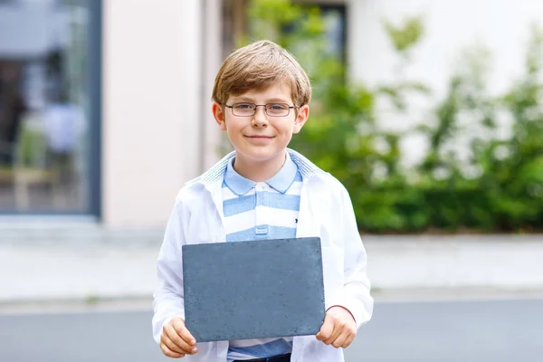 Niño feliz con gafas y mochila o mochila. Un colegial de camino a la escuela. Un niño sano y adorable al aire libre. Escritorio de tiza vacío en las manos para copyspace y texto libre. Regreso a la escuela. — Foto de Stock