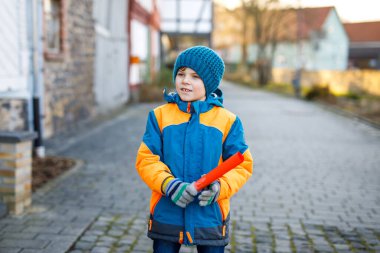 İlkokul çocuğu soğuk kış gününde okula yürüyordu. Mutlu çocuk şehir caddesinde eğleniyor. Renkli kış giysileri içinde sırt çantalı bir öğrenci proje için bir şeyler tutuyor.
