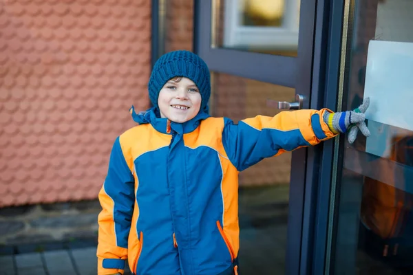 Kleine schooljongen van de lagere klas die naar school loopt op koude winterdag. Gelukkig kind in warme winterkleding deur naar school duwen, buiten. — Stockfoto