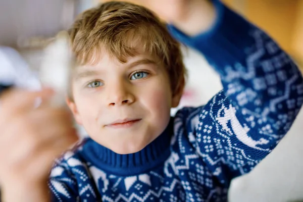 Liten pojke som tar ner julpynt från julgranen. Familj efter firande ta bort och kassera träd. Pojkar i festliga kläder med ren. — Stockfoto