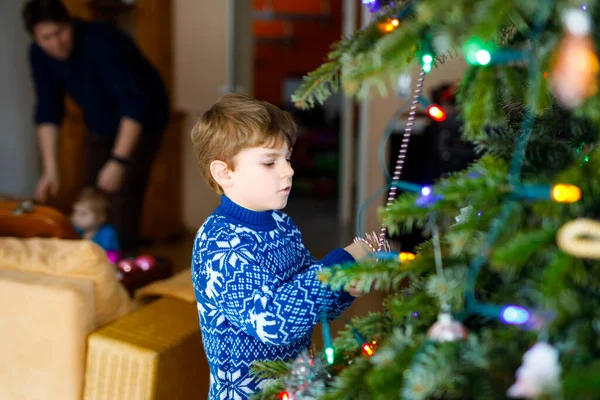 子供の男の子と彼の父親はクリスマスツリーから休日の装飾を取っています。背景に父親。祝いの後の家族は木を取り除き、処分する。トナカイとお祝いの服の男の子 — ストック写真