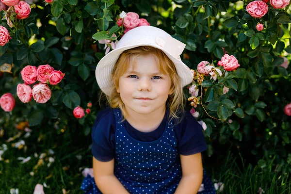 Portret van een kleuter in een bloeiende rozentuin. Schattig mooi mooi kind dat plezier heeft met rozen en bloemen in een park op zomerse zonnige dag. Gelukkig lachende baby. — Stockfoto