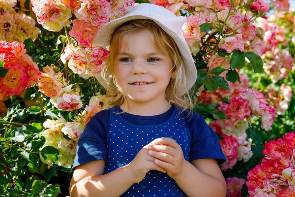 Портрет маленькой девочки в цветущем розовом саду. Симпатичный красивый милый ребенок веселится с цветами в парке в летний солнечный день. Счастливый улыбающийся ребенок. — стоковое фото