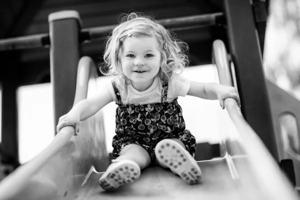 Linda niña jugando en la diapositiva en el patio al aire libre. Hermoso bebé en pantalones cortos de colores que se divierten en el soleado día cálido de verano. Niño deslizándose hacia abajo —  Fotos de Stock