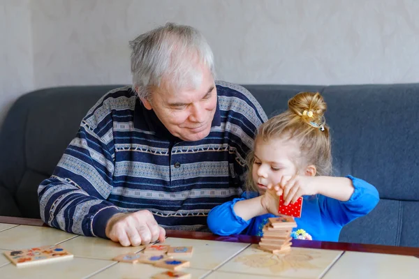 Beautiful toddler girl and grandfather playing together pictures memory table cards game at home. Cute child and senior man having fun together. Happy family indoors — Stock Photo, Image