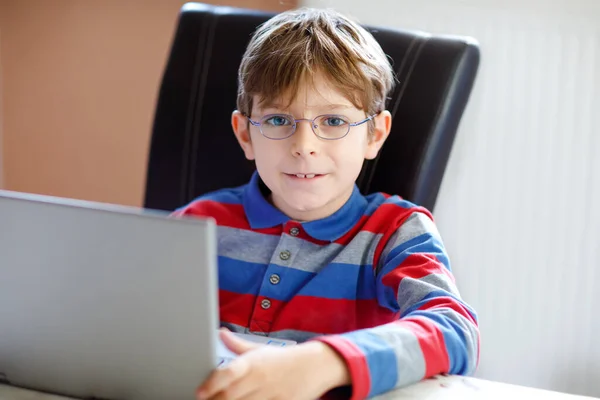 Счастливый здоровый мальчик с очками, делающий домашнюю работу дома с тетрадью. Заинтересованный ребенок пишет эссе с помощью Интернета. Концепция скрытых школьников — стоковое фото