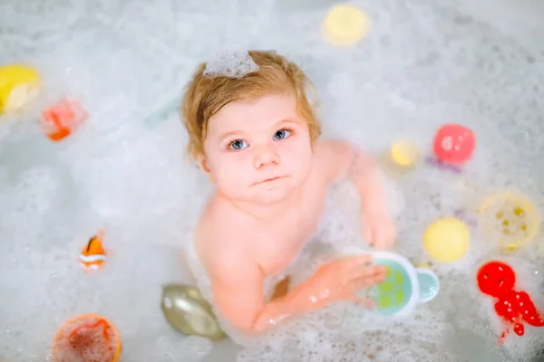 Linda menina adorável tomando banho espumoso na banheira. Criança brincando com brinquedos de borracha de banho. Criança bonita se divertindo com brinquedos coloridos de goma e bolhas de espuma — Fotografia de Stock