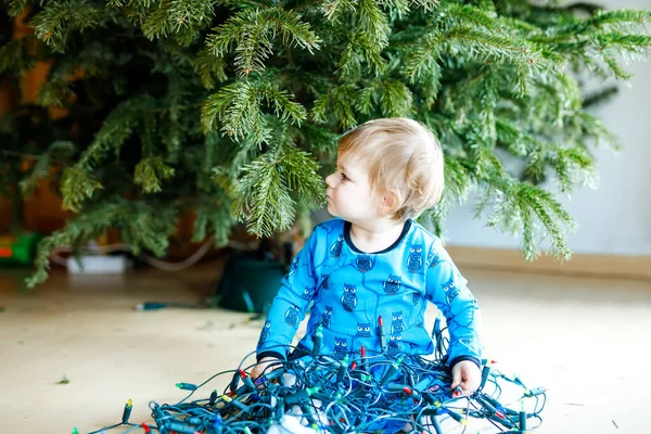 Nettes kleines Mädchen, das die Weihnachtsdekoration vom Weihnachtsbaum abnimmt. Kind mit Lichterkranz. Familie nach Feier Baum entfernen und entsorgen — Stockfoto