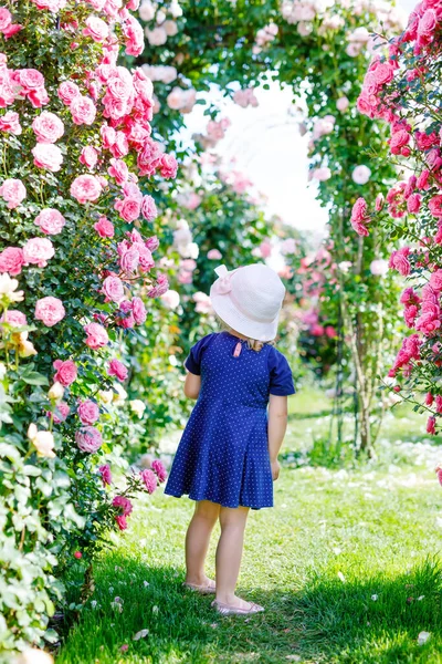 Portret van een kleuter in een bloeiende rozentuin. Schattig mooi mooi kind dat plezier heeft met rozen en bloemen in een park op zomerse zonnige dag. Gelukkig lachende baby. — Stockfoto