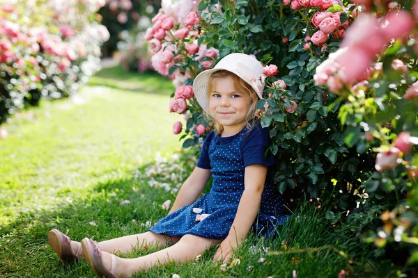 Retrato de menina pequena criança no jardim de rosas florescendo. Bonito linda criança se divertindo com rosas e flores em um parque no dia ensolarado de verão. Feliz bebê sorridente. — Fotografia de Stock