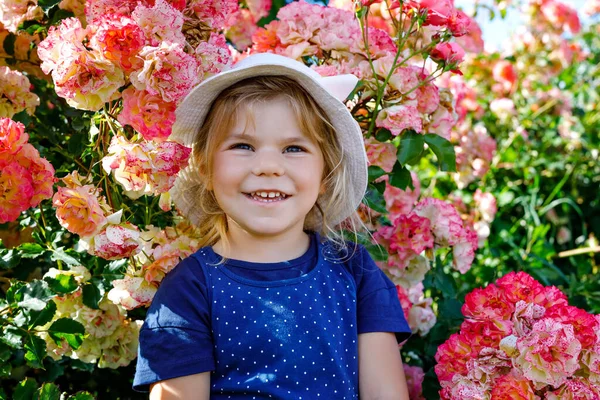 Портрет маленькой девочки в цветущем розовом саду. Симпатичный красивый милый ребенок веселится с цветами в парке в летний солнечный день. Счастливый улыбающийся ребенок. — стоковое фото