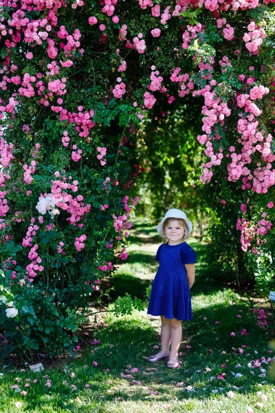 Ritratto di bambina in giardino di rose in fiore. Carino bello bel bambino divertirsi con rose e fiori in un parco in estate giornata di sole. Felice bambino sorridente. — Foto Stock
