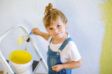 Sevimli küçük kız yeni evin rengiyle duvarı boyuyor. Aile onarım dairesi. Mutlu bebek duvarı boyuyor, paletle renk seçiyor, fırçayla eğleniyor, kapalı alanda.