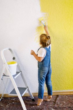 Yeni evin duvarını boyayan komik küçük kız. Aile onarım dairesi. Mutlu bebek duvarı boyuyor, paletle renk seçiyor, fırçayla eğleniyor, kapalı alanda.